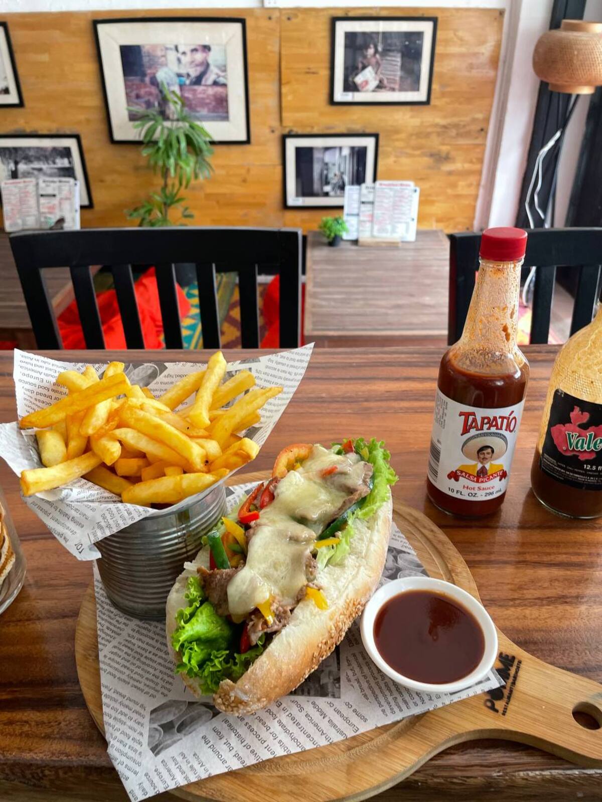 Steak melt baguette with melted cheese, peppers and onions, served with fries on a wooden table at Pomme Battambang